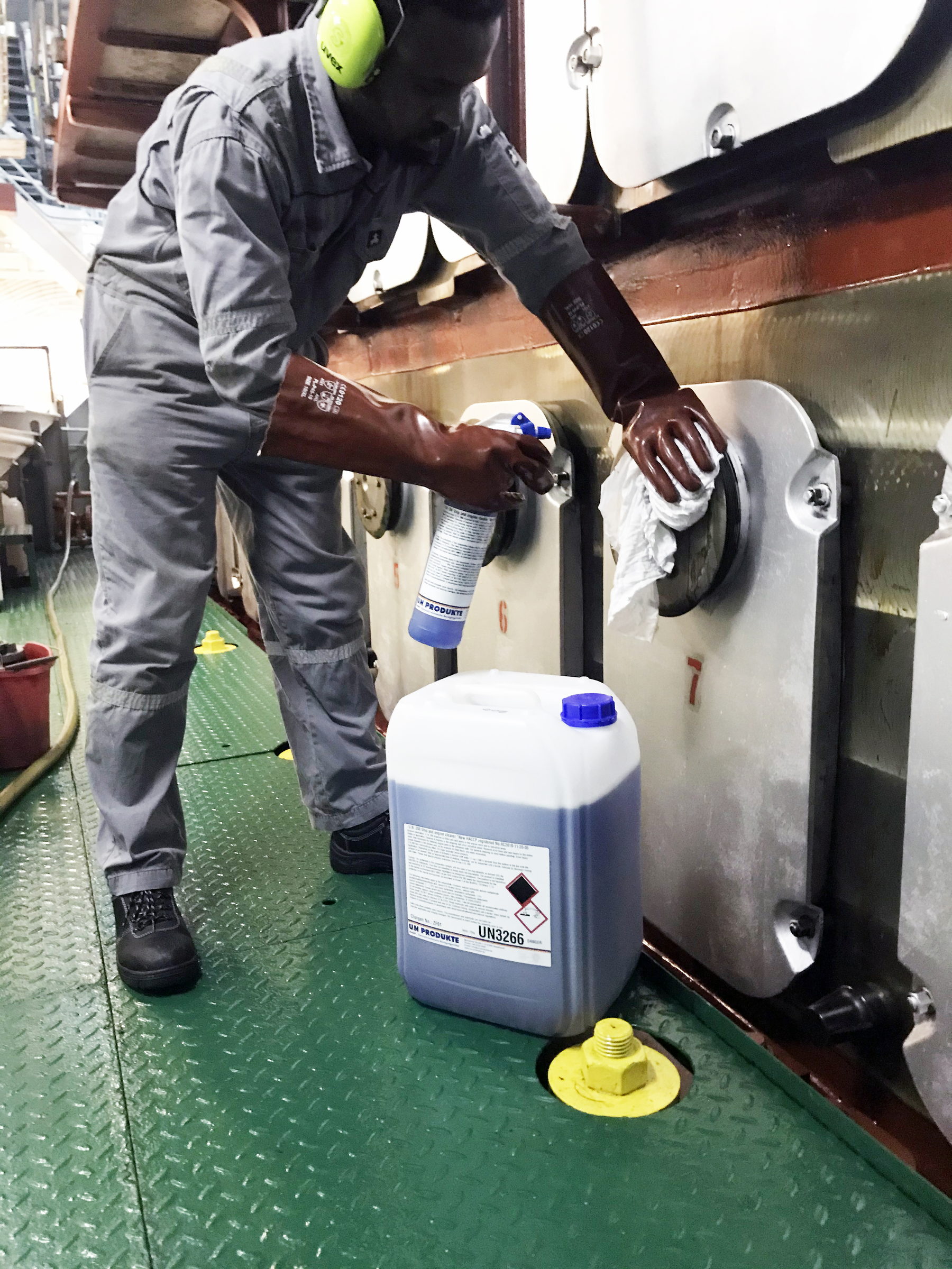 Crewmitglied setzt an Deck mit Kanister und Sprühflasche eine Reinigungslösung an